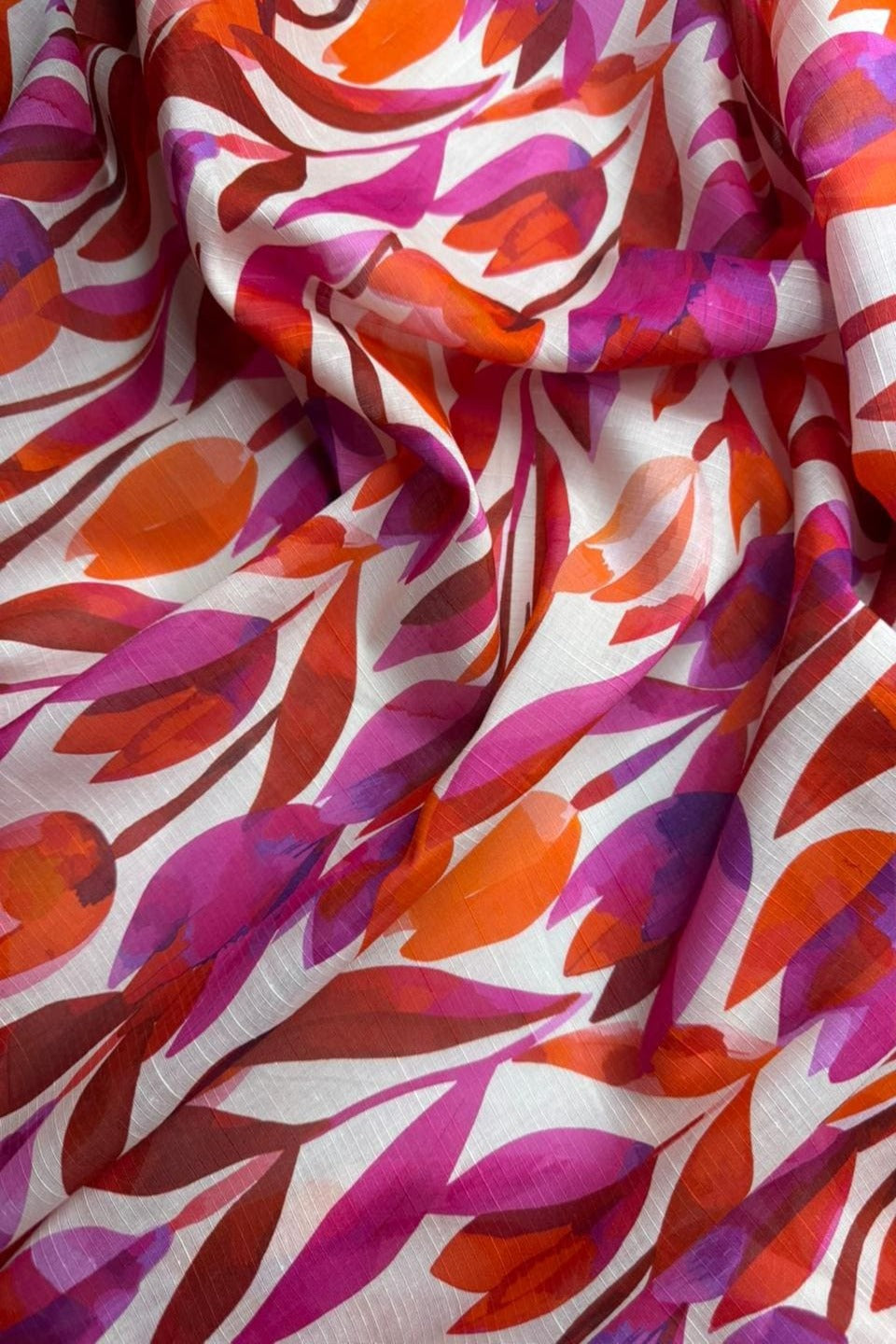 Colorful fabric with abstract leaf pattern in red, pink, and purple on a white background