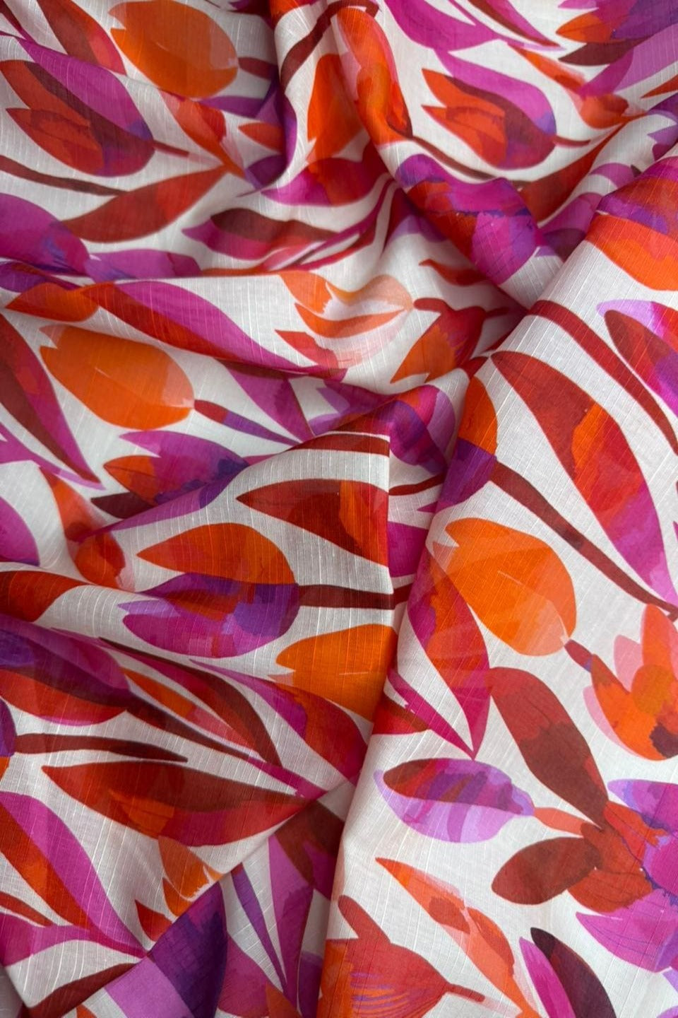Colorful fabric with abstract leaf pattern in red, pink, and orange on a white background