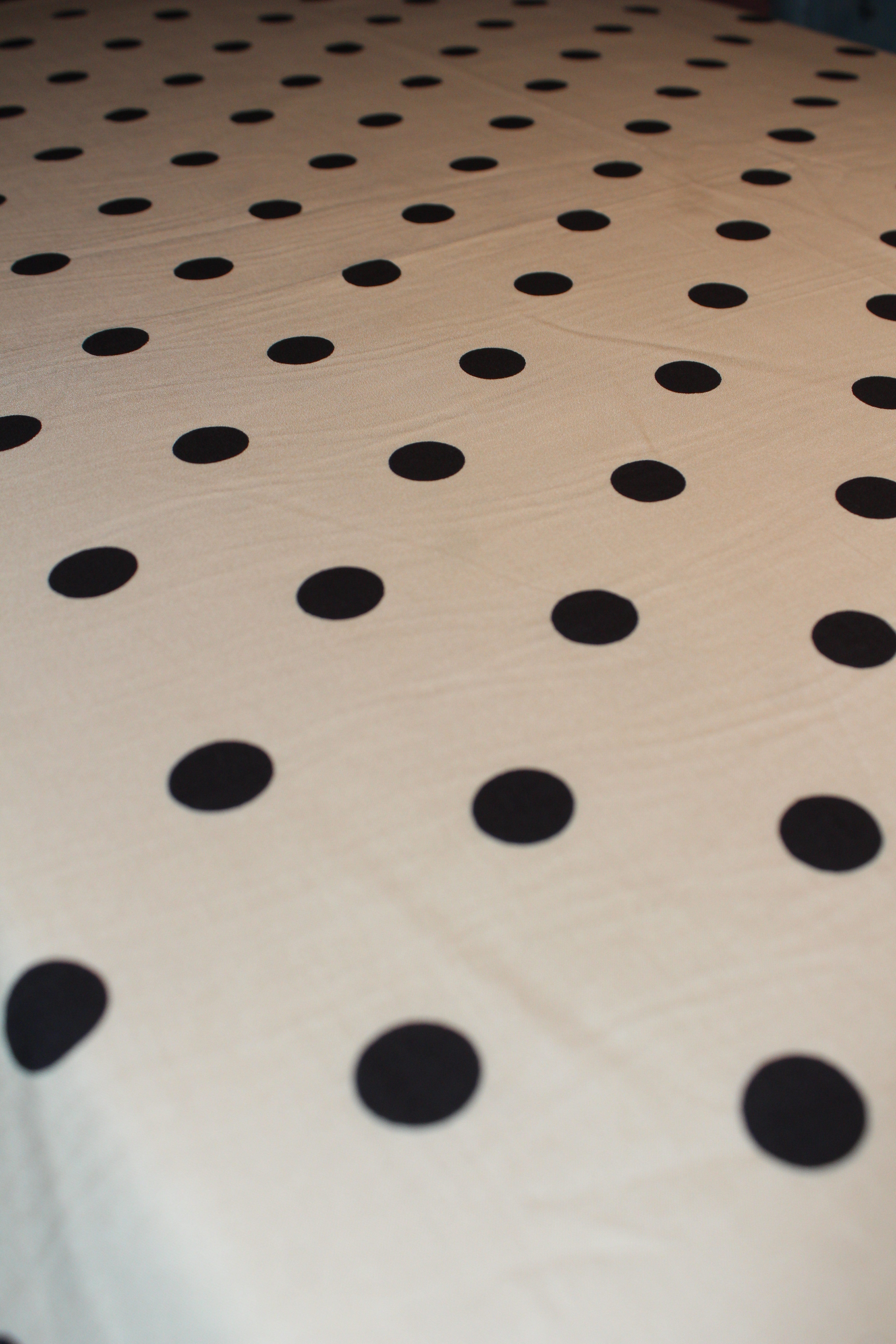 A close-up of a light beige or cream fabric surface with evenly spaced black polka dots, photographed at an angle.