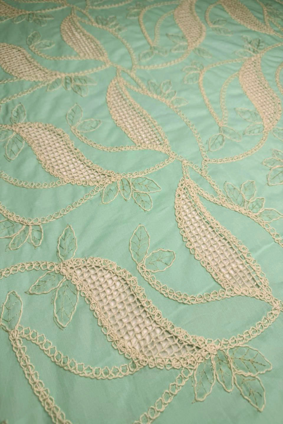 Close-up of embroidered fabric with leaf patterns on a light green background