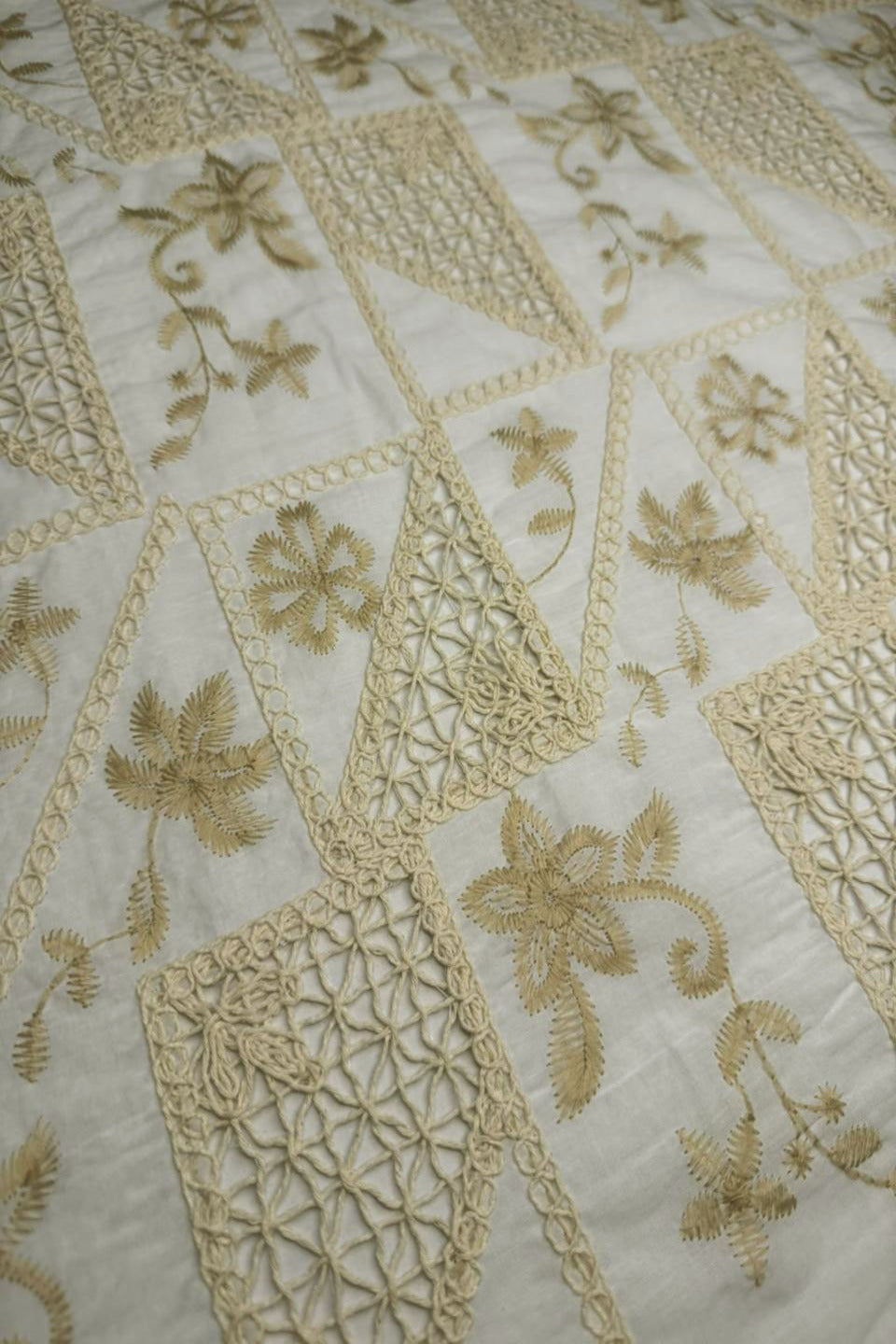 Close-up of embroidered fabric with gold floral patterns on a white background