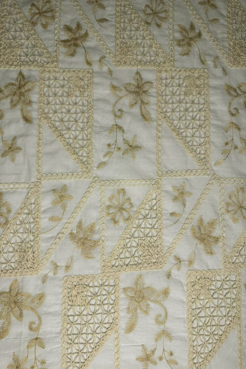 Close-up of a quilt with intricate gold embroidery on a white background