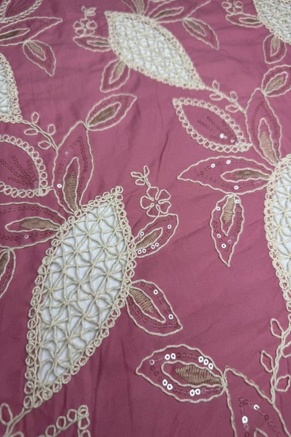 Close-up of a fabric with intricate floral embroidery on a pink background
