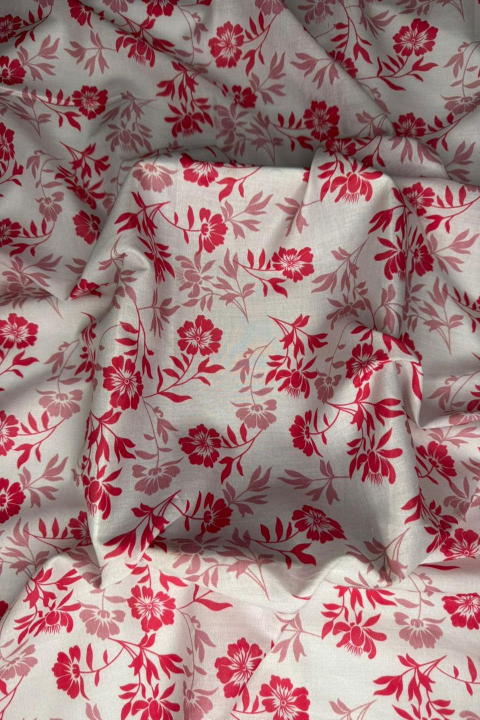 A close-up of draped fabric with an allover floral print in red and dusty pink on a warm off-white background.