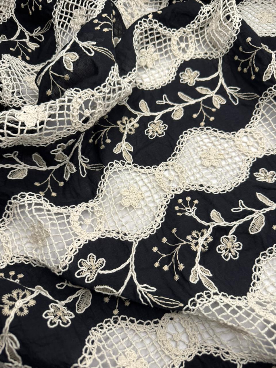 Close-up of black fabric with intricate white lace and floral embroidery