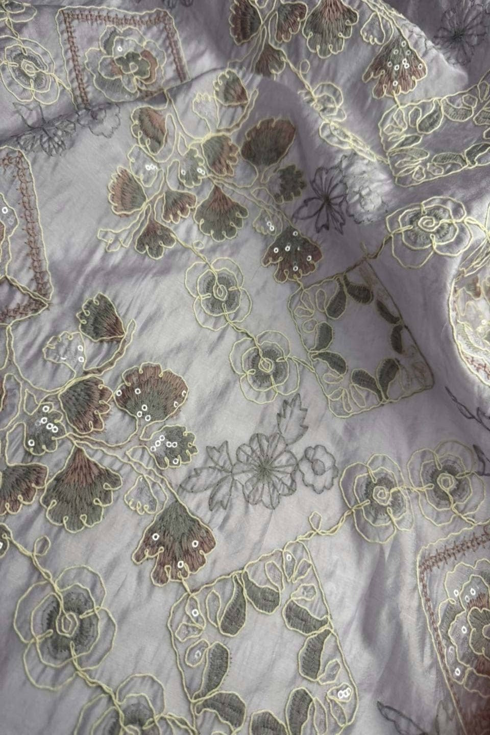 Close-up of embroidered fabric with floral patterns on a light purple background